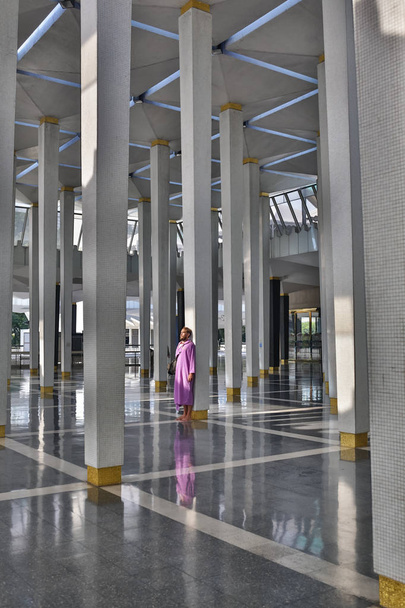 Мужчина турист в национальной мечети города Куала-Лумпур стоит рядом с колонной и наслаждается красотой интерьера
. - Фото, изображение