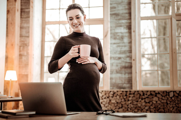 Nice pregnant businesswoman holding a cup with tea - Fotó, kép
