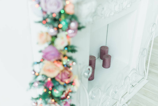 Christmas decor. Wreath decorated with Christmas balls. Interior. Candles pink. Photo zone with a fireplace. Burning light bulbs on the garland. - Photo, Image