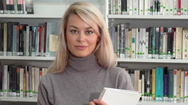 Όμορφη γυναίκα shushing στην κάμερα, κρατώντας το σωρό των βιβλίων της βιβλιοθήκης - Πλάνα, βίντεο