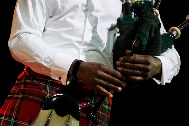 Een zwarte man in een wit overhemd en Schotse kilt houdt doedelzak. Multiculturele op een zwarte achtergrond.                               - Foto, afbeelding