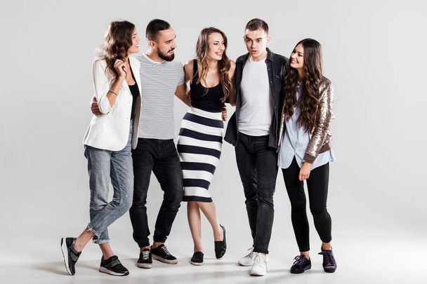 Company of friends in fashionable casual clothes stand together and talk on a white background in the studio - Foto, Bild