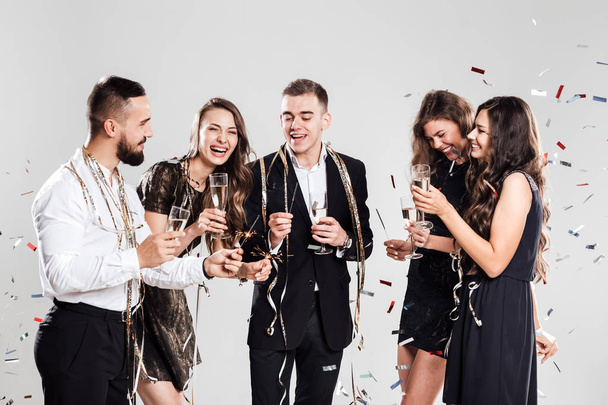 Company of  girls and guys dressed in stylish elegant clothes have fun together holding glasses of champagne and sparkles in hands on the white background confiture around. Party time - Fotografie, Obrázek