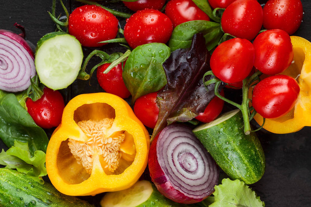 Divers légumes juteux mûrs avec des feuilles de salade sur une table noire humide
.  - Photo, image