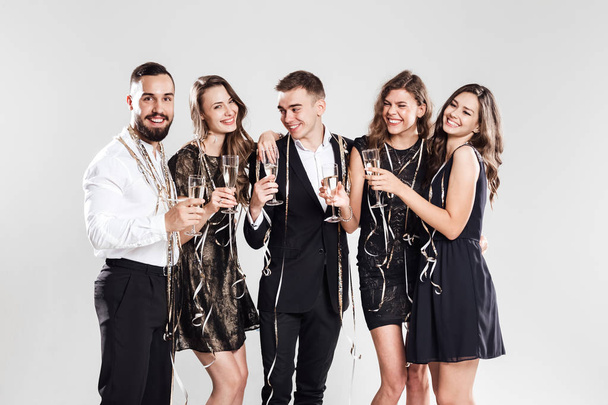 Girls and guys dressed in stylish elegant clothes smile together holding glasses of champagne and sparkles in hands on the white background confiture around. Party time - Φωτογραφία, εικόνα
