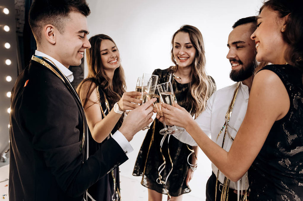 Company of happy friends dressed in stylish elegant clothes stand together and clink glasses with champagne. Party time - Foto, imagen