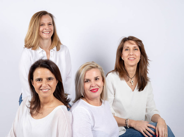 Grupo de 4 mujeres, amigas, de mediana edad divirtiéndose en una sesión de fotos en un estudio con fondo blanco, sentadas en una pelota
 - Foto, imagen