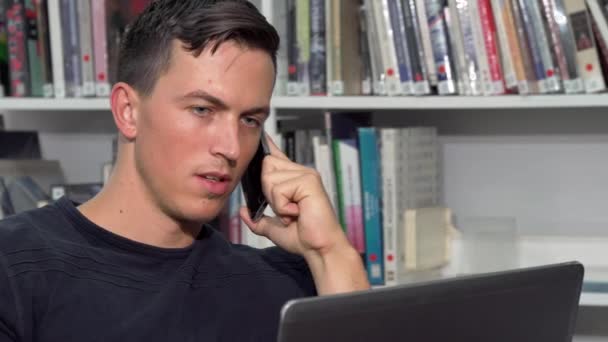 Hombre guapo hablando por teléfono, mientras hace la tarea en el portátil
 - Metraje, vídeo