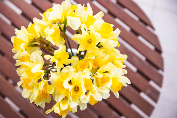 Ramillete de narcisos amarillos en un jarrón blanco sobre una mesa de madera al aire libre
 - Foto, Imagen
