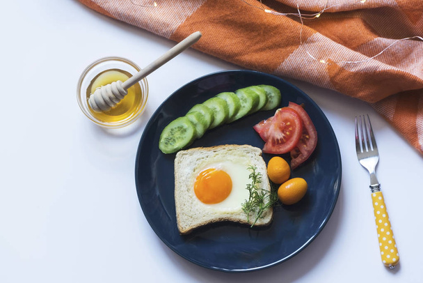Homemade egg in a hole with toast bread and vegetables on a blue ceramic plate with honey on a white background, above vantage poin photography, still life - Foto, afbeelding