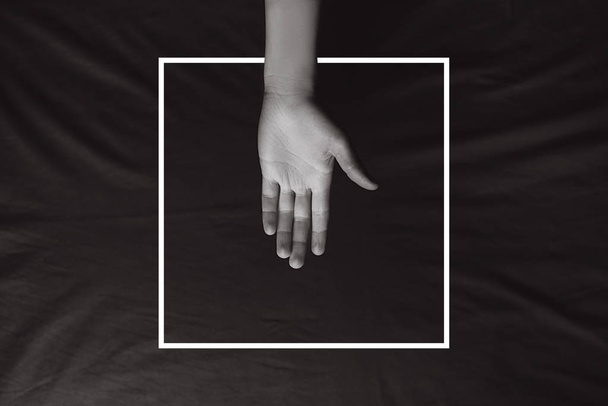 Female hand on the background of brown fabric with a drawn white frame. Minimal creative abstract concept. Flat lay. Copy space for text - Foto, Imagen