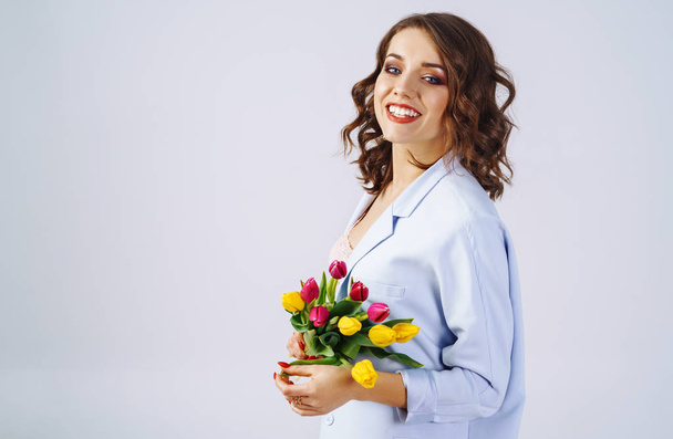 Fashion photo of a beautiful young woman with tulips in her hand .she dressed in a beautiful coat, and T-shirt with stripes.Spring concept. March 8. beautiful girl in stylish clothes - Φωτογραφία, εικόνα