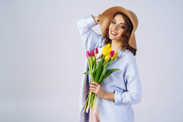 Fashion photo of a beautiful young woman with tulips in her hand .she dressed in a beautiful coat, and T-shirt with stripes.Spring concept. March 8. beautiful girl in stylish clothes - Foto, imagen