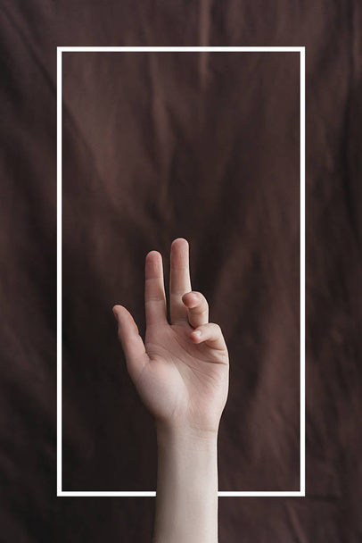 Female hand on the background of brown fabric with a drawn white frame. Minimal creative abstract concept. Flat lay. Copy space for text - Φωτογραφία, εικόνα