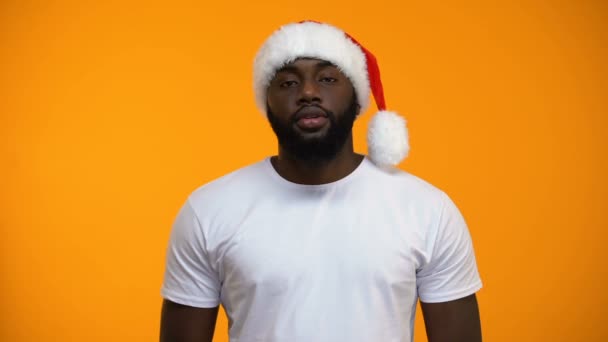 African-American man in Santa hat presenting Christmas gift, yellow background - Πλάνα, βίντεο