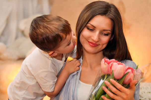 kleiner Sohn schenkt seiner Mutter einen Strauß zarter rosa Tulpen und küsst sie - Foto, Bild