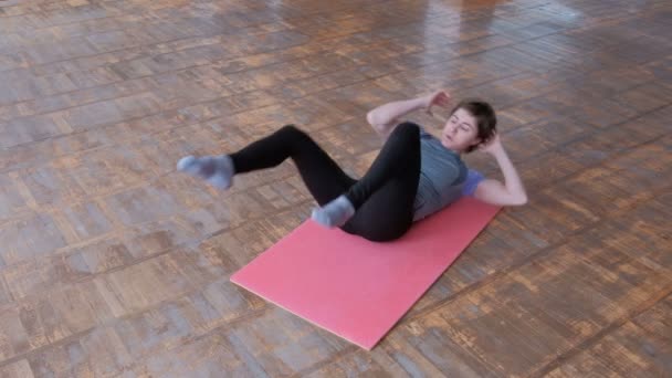 Ragazza sportiva sdraiata su un tappeto rosa esegue una serie di esercizi di fitness per rafforzare i muscoli addominali. Bodyflex. La camera con il vecchio parquet. Stile di vita Sport e salute
. - Filmati, video
