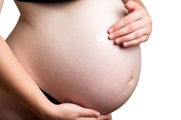 Um cosmético branco para estrias close-up em uma barriga branca é aplicado na pele da barriga das mulheres grávidas.
. - Foto, Imagem