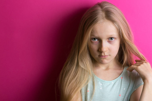 little beautiful girl blonde on a pink background looks into the camer - Fotó, kép