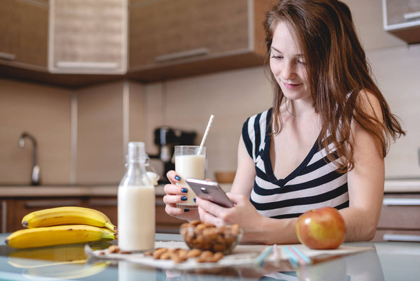 Donna che beve latte di mandorla biologico tenendo in mano un bicchiere in cucina. Bottiglia e frutta sul tavolo. Dieta prodotto vegetariano sano
 - Foto, immagini