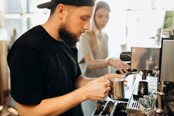 A stylish young man with beard,wearing casual clothes,cooks coffee in a coffee machine in a modern coffee shop. - Фото, зображення