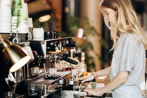 A young pretty thin blonde,dressed in casual outfit,is cooking coffee in a popular coffee shop. - Fotoğraf, Görsel