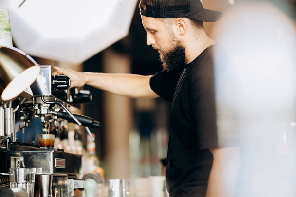 A stylish young man with beard,wearing casual clothes,cooks coffee in a coffee machine in a cozy coffee shop. - Fotó, kép