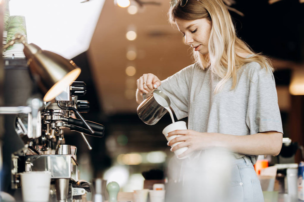 A good looking slim blonde with long hair,dressed in casual outfit,is cooking coffee in a modern coffee shop. Process of making coffee is shown. - Fotó, kép