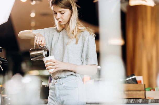A good looking slim blonde with long hair,dressed in casual outfit,is cooking coffee in a modern coffee shop. Process of making coffee is shown. - Fotó, kép