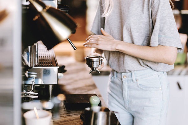 A good looking slim blonde with long hair,dressed in casual outfit,is cooking coffee in a modern coffee shop. Process of making coffee is shown. - Photo, Image