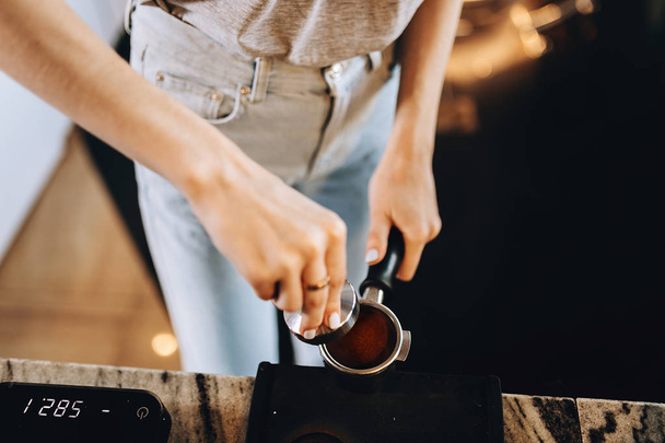 A young pretty slim girl,wearing casual outfit,is cooking coffee in a modern coffee shop. It focuses on the process. - Foto, afbeelding