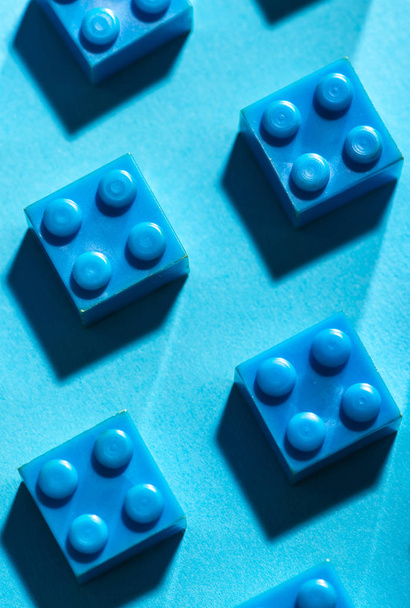 Blue unicolour plastic geometric cubes. Construction toys on geometric shapes paper multi colored background. Arranged in rows. Children's toy. Circle geometric shapes on plastic bricks.  - Foto, Bild