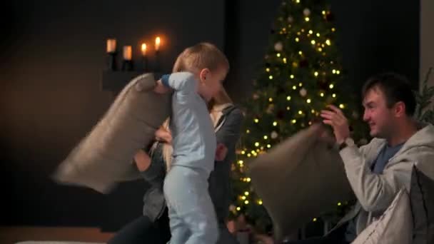 Yeni yıl önce Noel'de mutlu veliler oğulları pijama yatakta Noel'de bir yastık oturup iskambil ile mücadele - Video, Çekim