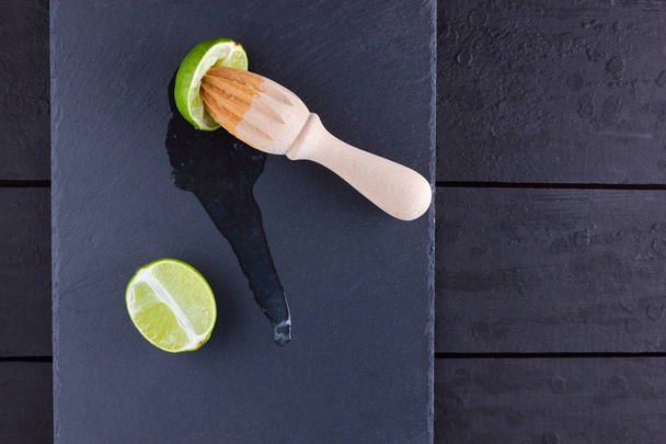 Lime halves and wooden juicer on a slate board. Lime on a black background. Fresh lime juice flows over the stone board. Healthy food - Foto, Imagen