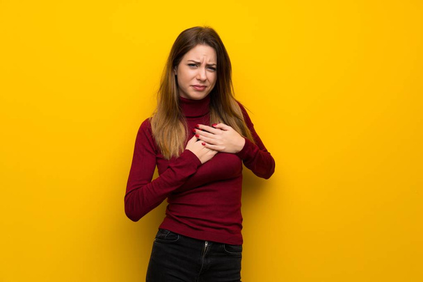 Frau mit Rollkragen über gelber Wand hat Schmerzen im Herzen - Foto, Bild