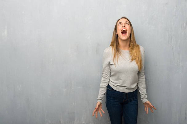 Mujer joven en la pared texturizada gritando al frente con la boca abierta
 - Foto, imagen