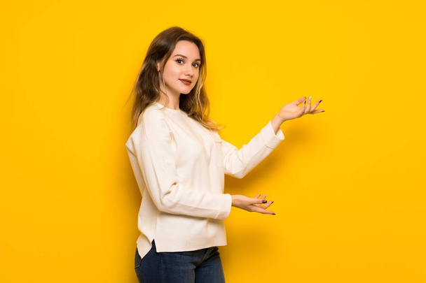 Adolescente chica sobre amarillo pared extendiendo las manos a un lado para invitar a venir
 - Foto, Imagen