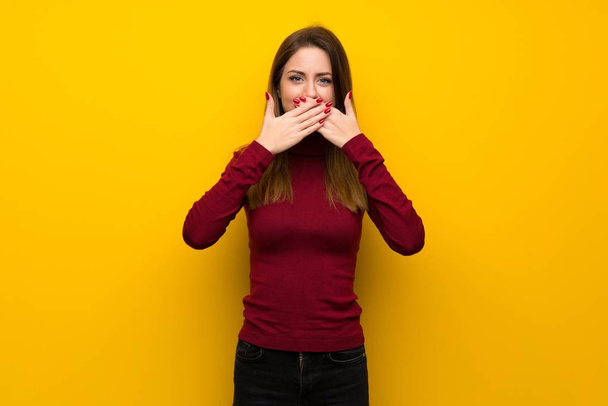 Женщина с водолазкой над желтой стеной покрывает рот руками за то, что сказала что-то неуместное.
 - Фото, изображение