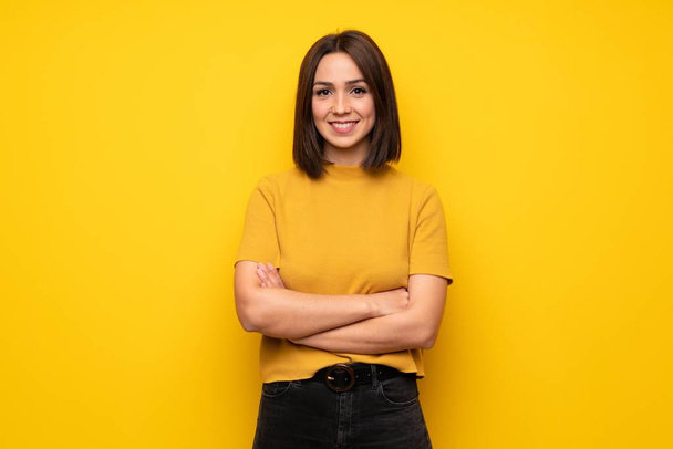 Jovem mulher sobre a parede amarela mantendo os braços cruzados na posição frontal
 - Foto, Imagem