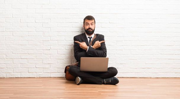 Бізнесмен зі своїм ноутбуком, що сидить на підлозі, вказуючи на латеральні сумніви
 - Фото, зображення