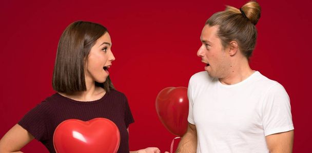 Valentin napi meglepetés és döbbent arckifejezés, piros háttér felett pár - Fotó, kép