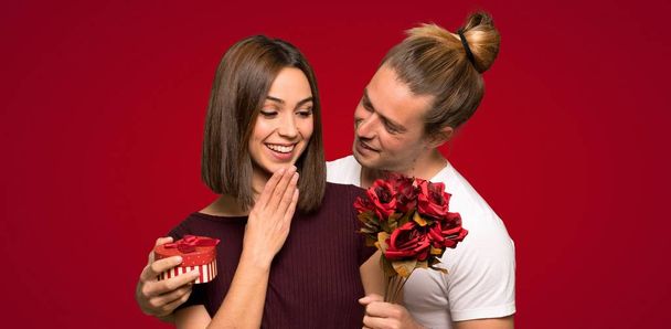 Пара в День Святого Валентина с цветами и подарками на красном фоне
 - Фото, изображение