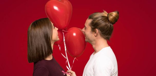 Casal no dia dos namorados com balões com forma de coração sobre fundo vermelho
 - Foto, Imagem