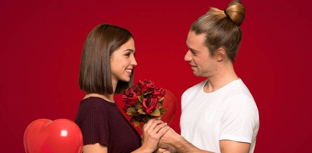 Pareja en día de San Valentín con flores sobre fondo rojo
 - Foto, Imagen