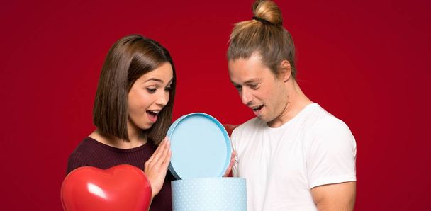 Couple in valentine day holding gift box in hands over red background - Foto, Imagem