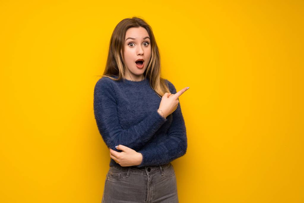 Teenager girl over yellow wall surprised and pointing side - Photo, Image
