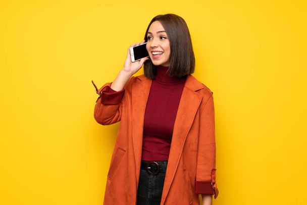 Νεαρή γυναίκα με το παλτό που κρατά μια συνομιλία με το κινητό τηλέφωνο - Φωτογραφία, εικόνα
