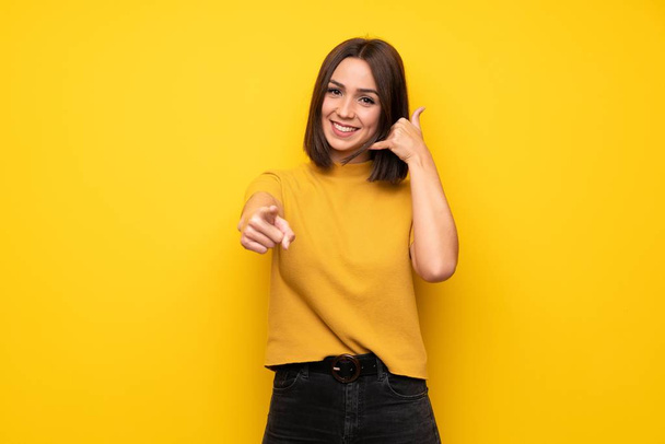 Young woman over yellow wall making phone gesture and pointing front - Photo, Image