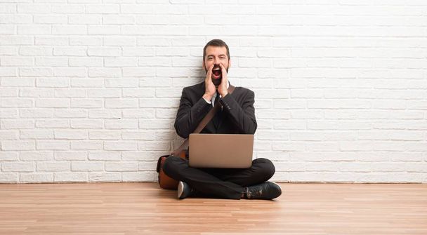 Businessman with his laptop sitting on the floor shouting and announcing something - Photo, Image