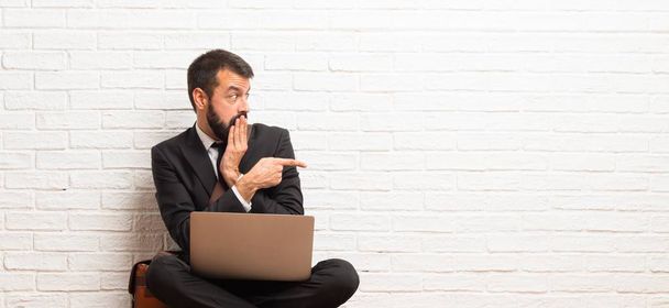 Biznesmen z swojego laptopa, siedząc na podłodze palcem wskazującym na bok ze zdziwieniem - Zdjęcie, obraz